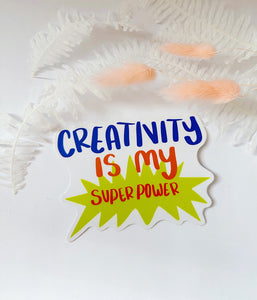 Sticker with white background that reads “creativity is my super power” in colorful letters over a bright green burst shape