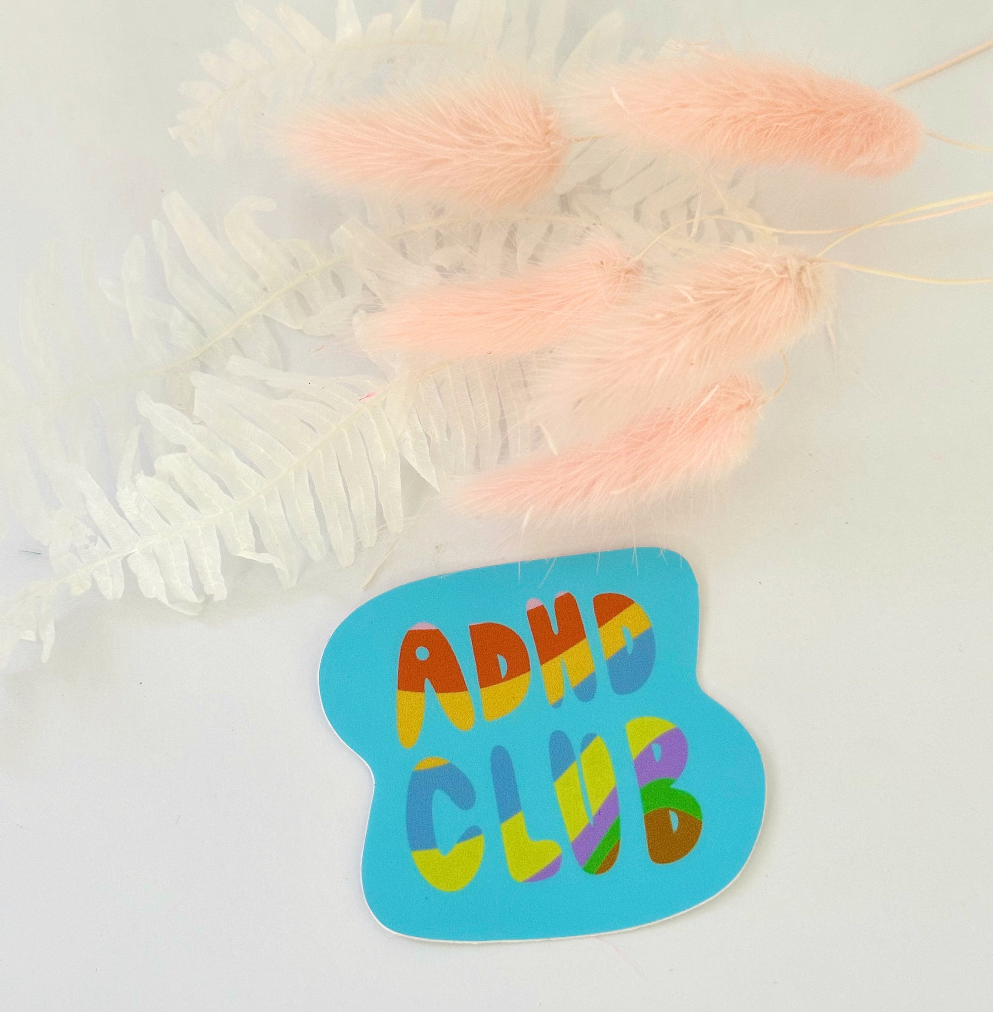 Blue green sticker that reads “adhd club” in colorful letter